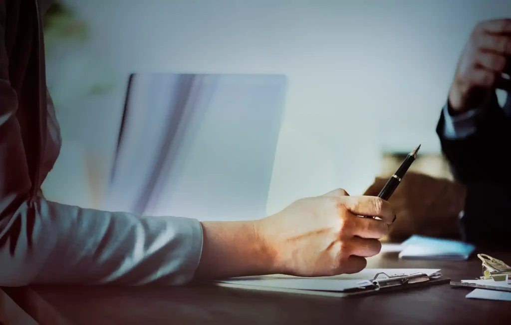 Persona sosteniendo pluma revisando documentos en escritorio