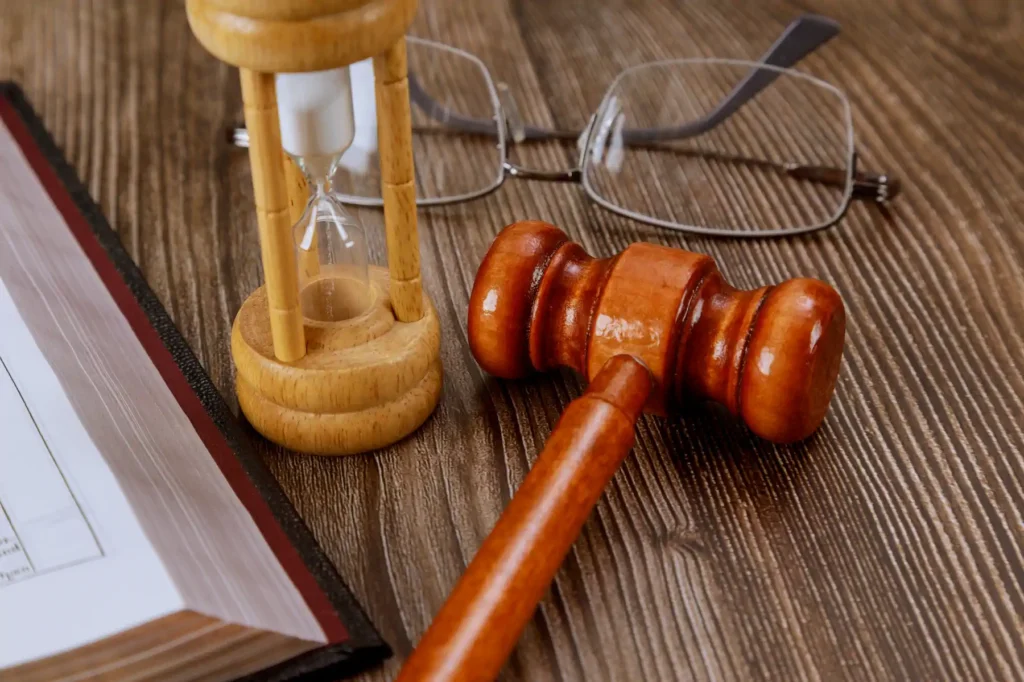 Mazo judicial, reloj de arena, lentes y libro sobre madera
