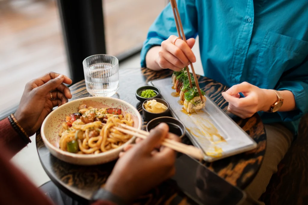 Dos personas compartiendo sushi y fideos udon en restaurante japonés