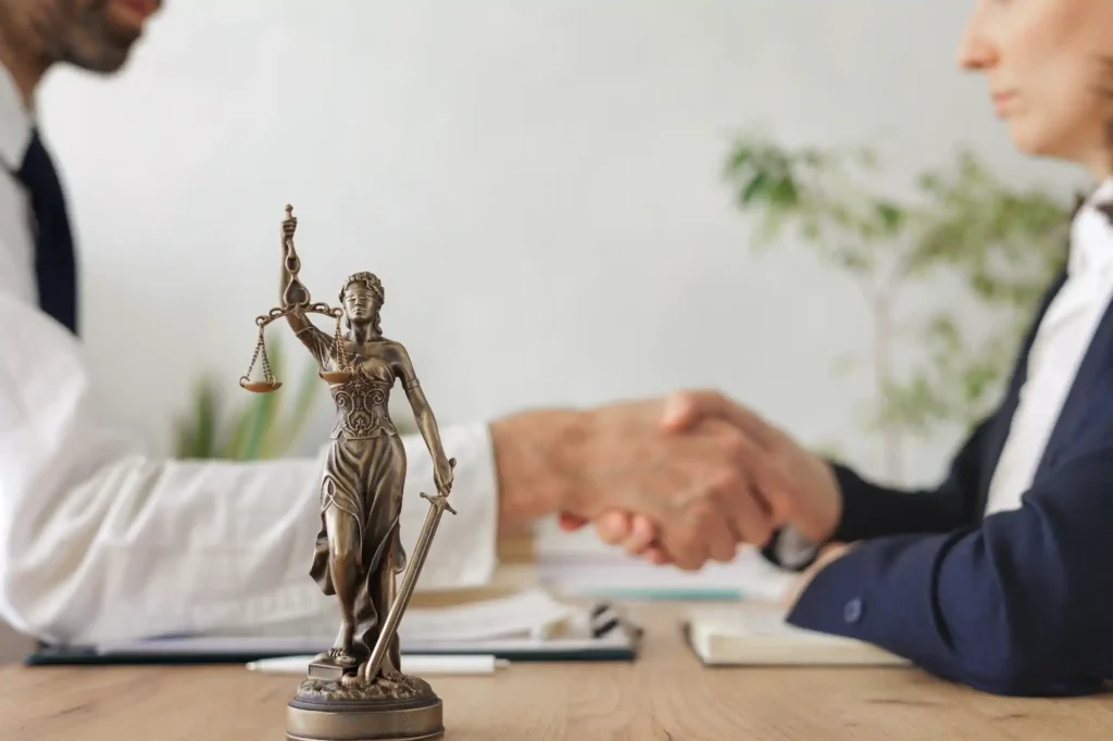 Estatua de la Justicia en escritorio con apretón de manos legal