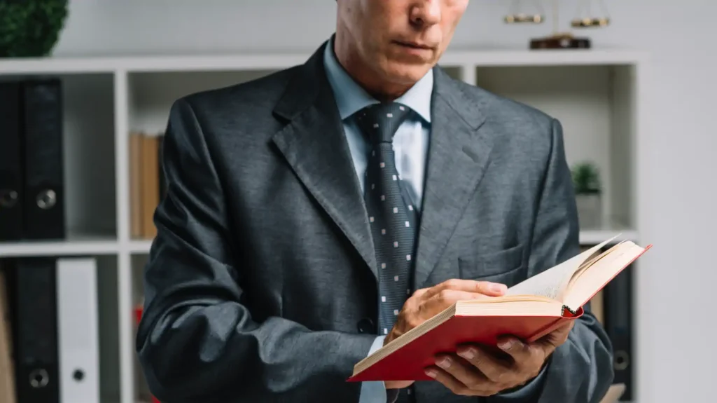 Abogado de traje leyendo un libro rojo en oficina