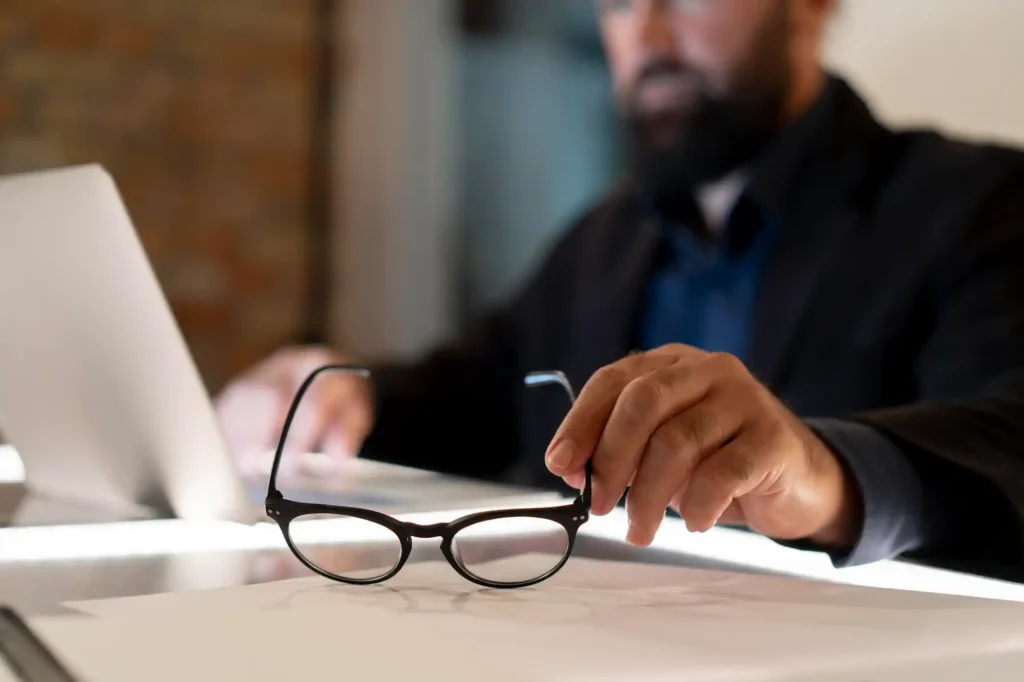 Hombre de negocios tomando lentes sobre escritorio con laptop