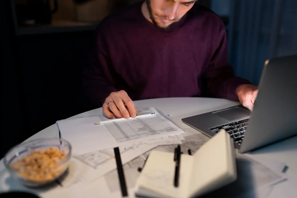 Hombre revisando documentos financieros junto a laptop de noche