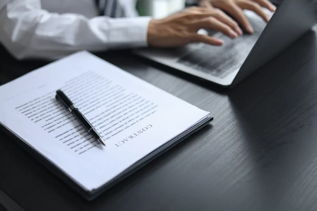 Professional reviewing a contract with a pen and laptop at a desk